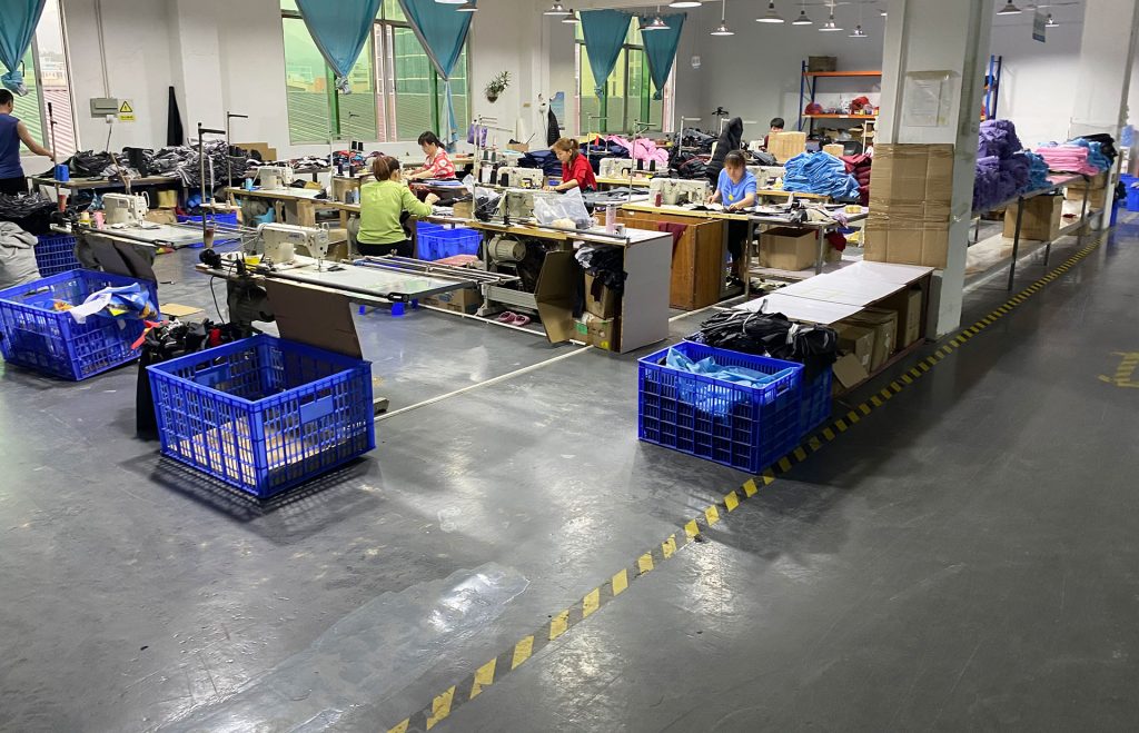 Umbrella sewing workshop with workers, fabric bundles and blue storage crates.